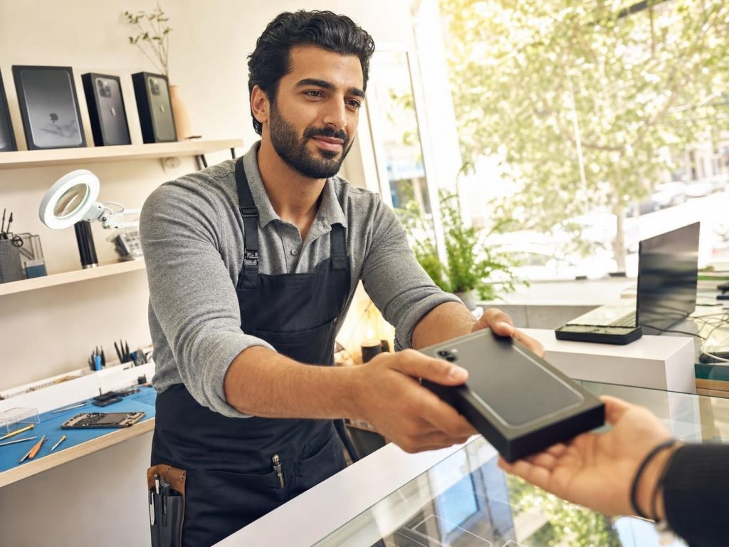 Technicien d'atelier remettant un téléphone de prêt à un client au comptoir d'une boutique de réparation smartphone